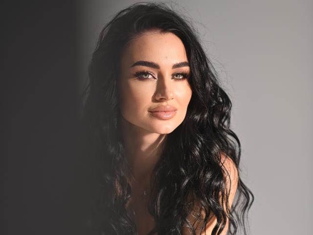 LuneSauvage has wavy black hair, full lips, and a sexy face with sultry eyes and thick eyebrows. She's looking at the camera with a slight, seductive smile.