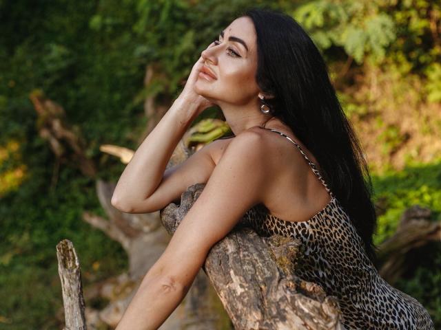LuneSauvage with long black hair, wearing a leopard-print dress, resting her chin on a tree, showing her slim arms and subtle tattoos, with a confident, sexy smile.