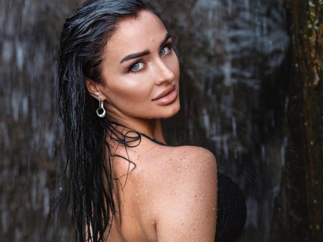 LuneSauvage with wet black hair, glistening skin, and blue eyes, wearing a black strapless top, looking over her shoulder, showing her tits, with a silver earring.