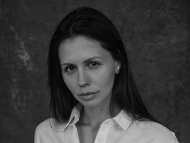 MashaSmithh has dark, straight hair, a serious expression, and wears an unbuttoned white shirt. Her small tits are visible. Black and white portrait.