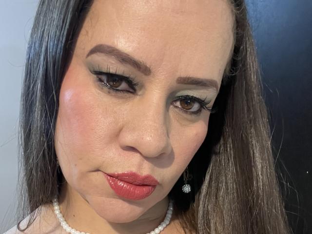 CharllotI has a fat ass face with red lips, brown eyes, and long black hair. She's wearing a pearl necklace and has green eyeshadow with thick black eyelashes.
