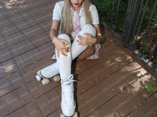 ValerieBunny sitting on wooden deck, wearing white skater shoes, pink plaid shirt, white knee socks, and holding knees. Her blonde hair and red lips are visible.
