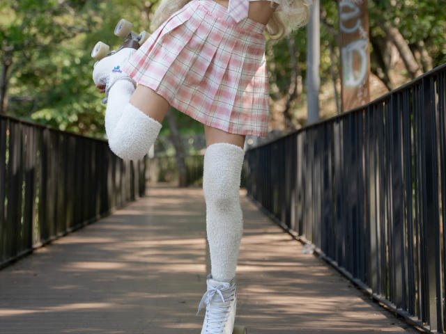 ValerieBunny's pink plaid skirt, white thigh-high socks, and white sneakers with a small blue sticker on her bike, mid-air on a black metal bridge.