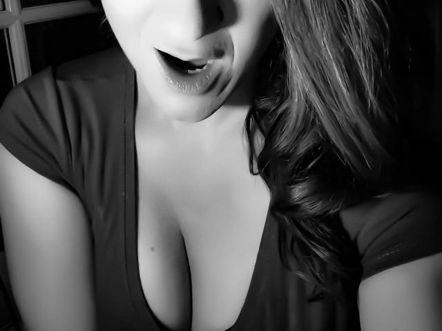 Black-and-white photo of MissGinger's face and chest, showing her full tits and slightly parted lips with a seductive expression, her wavy hair falling to the side.
