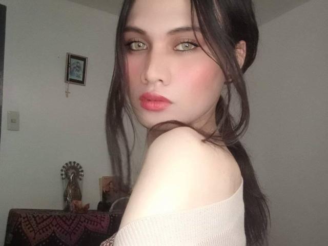 AmberH with pale skin, green eyes, and pink lips, has dark brown hair in a ponytail, wearing an off-shoulder white top, showing her bare shoulder and slightly turned face.