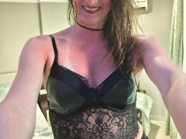 LucieDeluxe-hot with wet brown hair, smiling, wearing a green satin bra with black lace and a black choker, showing her tits and lace-covered belly in a selfie.