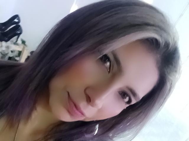 Michelle Dumont hat hellbraune Augen, eine kleine Nase und ein sanftes Lächeln. Sie hat dunkelviolettes Haar mit blonden Strähnen und einen dezent rosafarbenen Schimmer auf ihren Wangen..