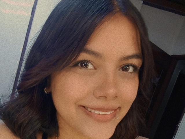 EmilyRoberts has dark brown hair, brown eyes, and a small smile with a visible lower lip piercing. Her light skin is smooth, and she's wearing small earrings.