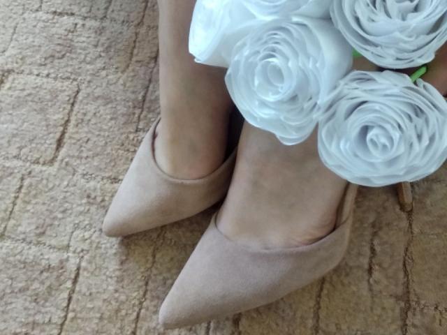 Les pieds de Nurri sont chaussés de chaussures pointues en daim beige avec un bouquet de roses blanches sur le dessus, sur un fond de sol recouvert de tapis. Doux, féminin, élégant..