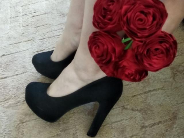 Le gambe pallide di Nurri, indossava tacchi alti neri, teneva un bouquet di rose rosse, posizionato vicino ai suoi piedi su un pavimento tappezzato..