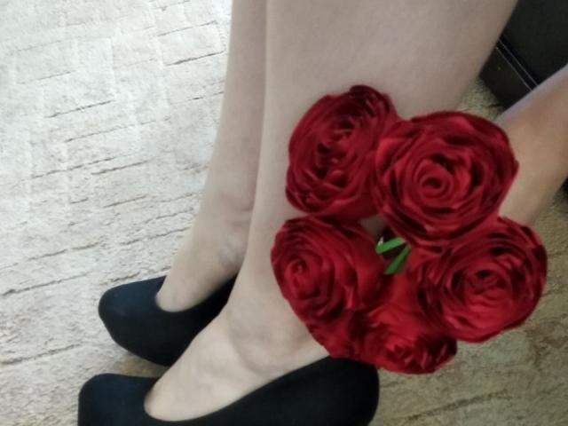 Las piernas pálidas de Nurri, con un ramo de rosas rojas descansando sobre sus pies, vestía zapatos planos negros sobre una alfombra beige..