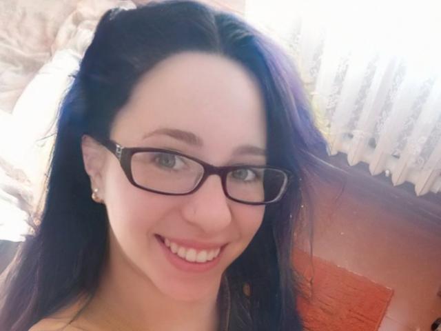 AlinaMiss has long dark hair, glasses, and is smiling with white teeth. She has fair skin, small earrings, and is looking at the camera with a cute face.