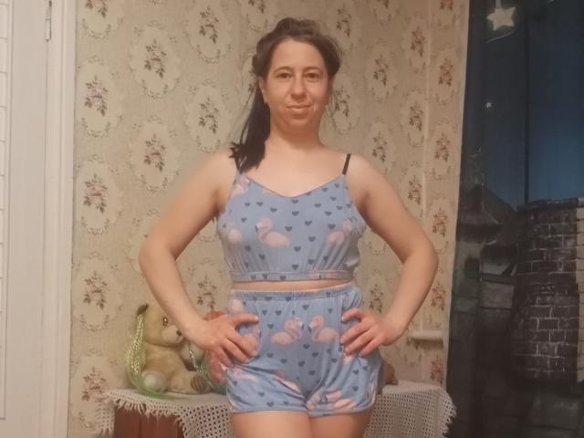 AlinaMiss with hands on hips, wearing blue floral sports bra and shorts, standing in room, smiling, black hair in ponytail, pale skin, small tits, cute, relaxed, confident.