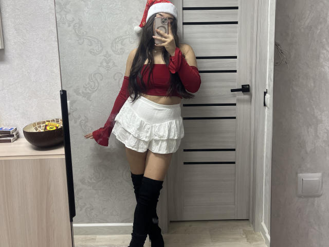 CrystalCharm wearing a red crop top, white frilled skirt, red gloves, black knee-high boots, and a Santa hat, taking a mirror selfie with long dark hair, showing her ass.