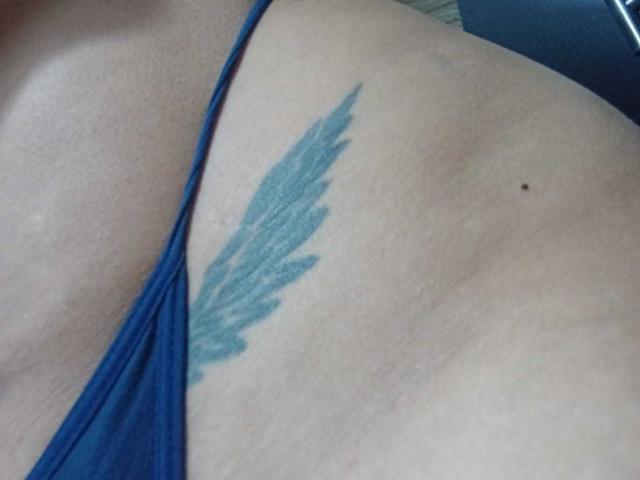 DaisyFx's lower torso with a blue feather tattoo just above her blue thong, showing light skin and a small black mole on her right side.