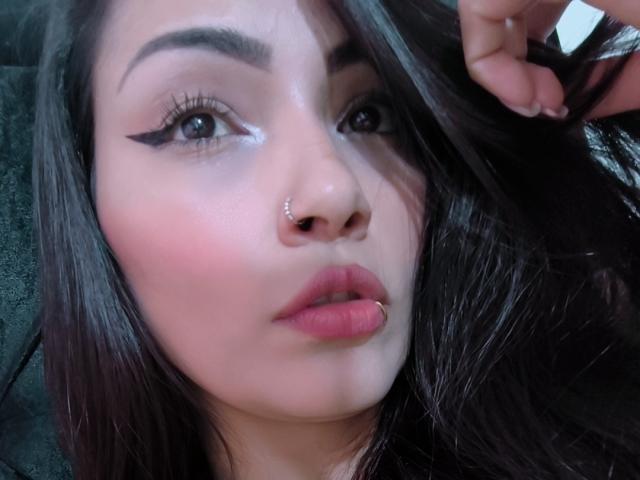 AliceGiorgia's face with dark brown hair, a nose ring, thick black eyebrows, winged eyeliner, pink blush, and a lip ring. Her skin is light, and her lips are slightly parted.