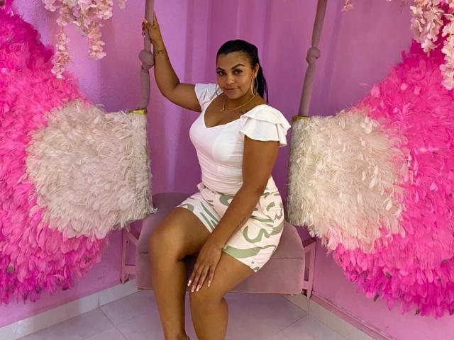 BrunetteScarlet with dark skin and curvy ass, wearing a white ruffled top and green patterned skirt, sitting on a pink swing with fluffy pink and white wings.