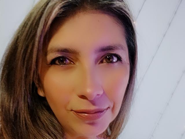 MichelleDumont a les yeux marron, les cheveux bruns et lisses, et un sourire discret avec les lèvres légèrement entrouvertes. Son visage est au centre de l'image. Elle a un petit nez et elle est jolie..