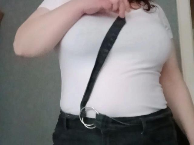 Feuchtundgeil-hot in a white t-shirt with visible nipples, black suspenders, and black pants, holding the top of the suspenders with one hand.
