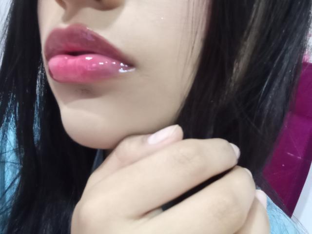 OdettePrincess's glossy pink lips are slightly parted, showing a bit of shiny saliva. She's holding her chin with a hand, her black hair partially visible.