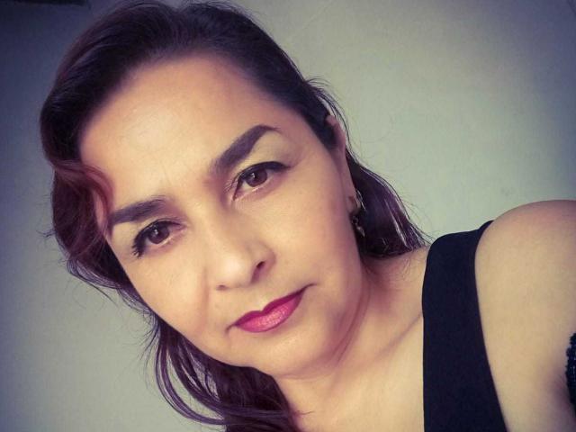 YaraStone ha gli occhi marrone scuro, le sopracciglia folte e il rossetto rosa. Indossa una maglietta nera, i capelli castani leggermente ondulati, e ha un piccolo sorriso sul viso..