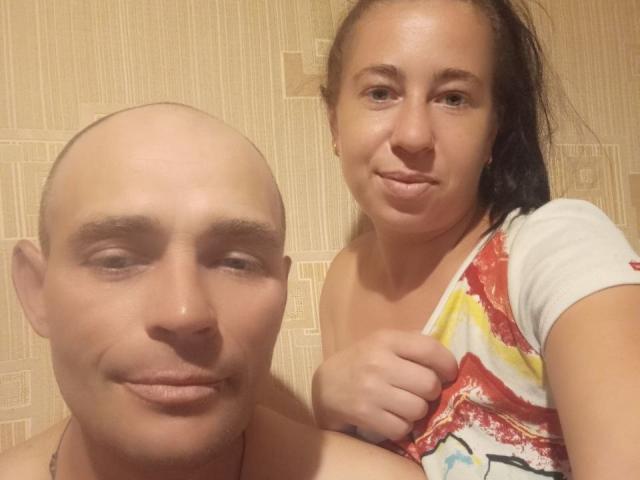 TonyAlina con la cabeza calva y TonyAlina con el pelo castaño, sonriendo, sosteniendo una camisa de colores, mostrando los pezones, de pie juntas, hombros desnudos, piel clara, iluminación cálida, selfie informal..