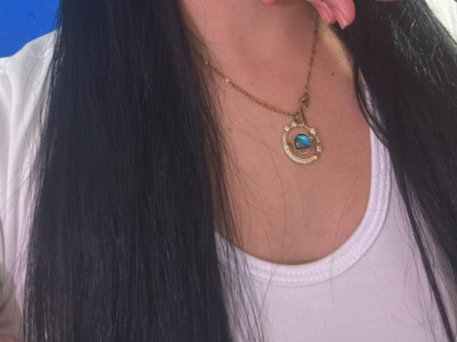 SarahGood's black hair, white shirt, and gold necklace with a blue gem. Her tongue slightly out. Boobs visible under shirt, no other body parts shown.