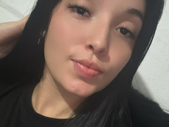SarahGood has a cute face with shiny black hair, light skin, and puffy pink lips. She's looking at the camera with a slight smile, wearing a black shirt.