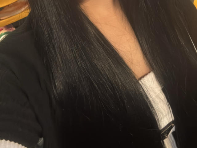 SarahGood's long black hair, shiny and straight, covers her white-clothed chest, with a black shirt partially visible, showing a small bit of her tan skin.