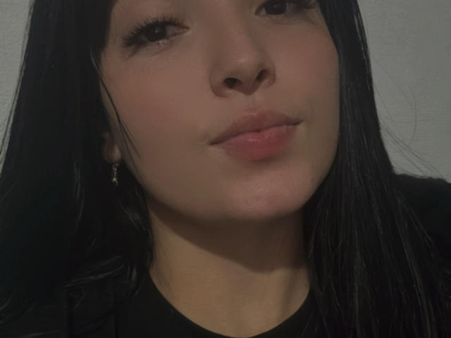 SarahGood has a cute face with glossy pink lips, straight black hair, and small earrings, looking slightly to the side with a subtle smile. Her skin is fair.