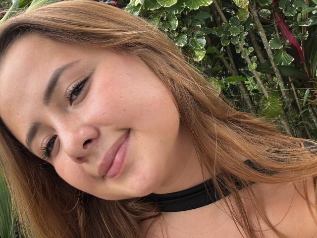 NatSorian has light brown hair, a slight smile, and is wearing a black choker. She's a cute, freckled bitch with subtle makeup and relaxed, natural beauty.