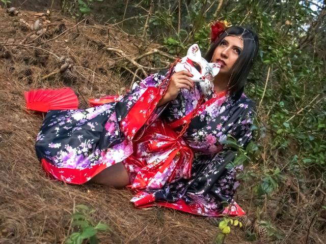 EvangelineAx with black hair, floral kimono, red obi, and red hand fan, sitting on brown pine needles, holding a white mask, looking up, with a red flower in hair.