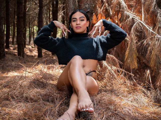 IrinaFerrero, sitting in pine forest, wearing black turtleneck sweater, exposing tan lines, black thong, bare feet, arms raised, confident expression, dark hair, light brown skin, attractive.