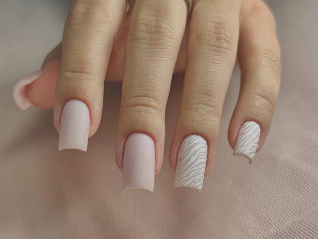 Skendi's pink-manicured nails with a white, wavy-patterned nail on the ring finger. Her fingers are slightly spread, showing off the detailed nail art.