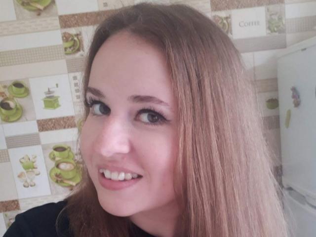 RosaJillian has light brown hair, blue eyes, and a cute smile. She's wearing black, with long eyelashes and pink lipstick, showing a pretty face.