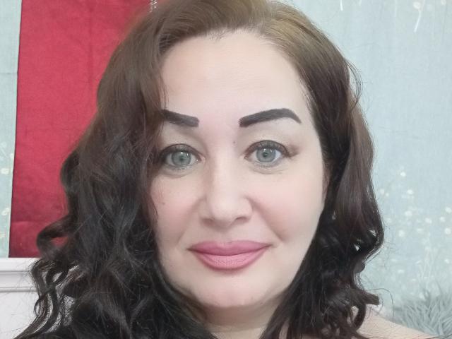 LexyRose has curly black hair, thick black eyebrows, blue eyes, pink lipstick, and a slight smile. Her face is centered, showing a fair skin tone.