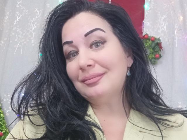 LexyRose has black, wavy hair, brown eyes, and thick eyebrows. She's smiling with pink lips, wearing a yellow shirt, and has small earrings. Her tits are not visible.