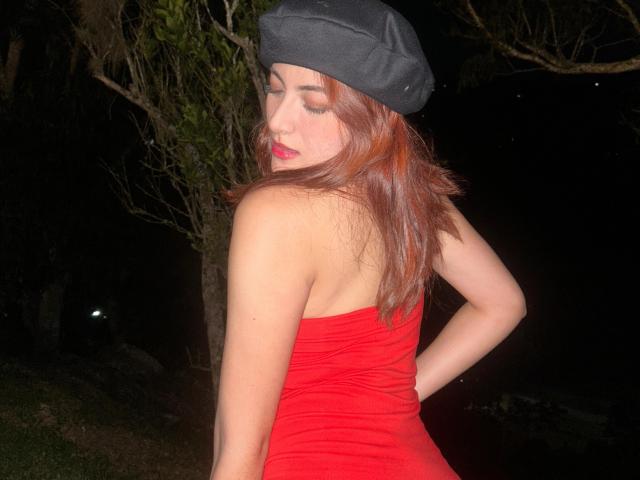 SpencerLe with red dress, bare back, and black beret, showing ass, looking back with eyes closed, red lipstick, brown hair, night setting, tree in background.