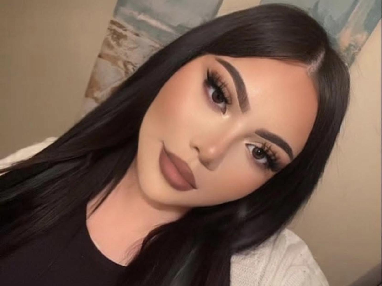 PrincessDollyLee has long black hair, thick eyebrows, long eyelashes, and full, matte brown lips. She's wearing a black top with a white cardigan.