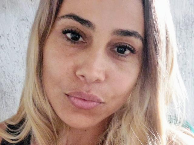 MaturesSugar69 has light brown skin, blonde hair, thick eyebrows, long eyelashes, and pink lips in a slight pout. She's looking straight at the camera with a neutral expression.