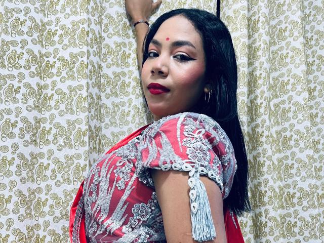 KalindaSajanii with medium tits, wearing a red and silver embroidered traditional outfit, red lipstick, and a bindi, has long black hair, raising her arm, looking over her shoulder.