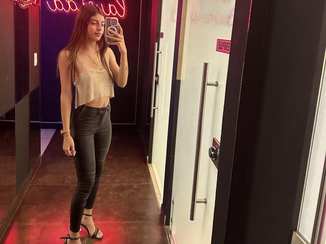 CiaSweet mit langen braunen Haaren, die ein glitzerndes, ärmelloses Top, schwarze Lederhosen und schwarze High Heels trägt, macht ein Selfie vor einem Spiegel und zeigt dabei ihre schlanke Figur und ihr kleines Hinterteil..