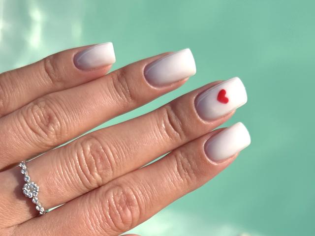 Karish's pale pink manicured nails with a small red heart on the middle finger, wearing a silver ring with diamonds on her left hand.