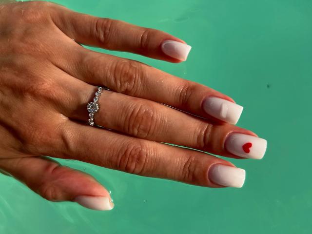 Karish's hand, met nagels in een roze en witte French manicure, een rode stip op één nagel, en een zilveren ring met kleine diamanten, drijvend in groen water..