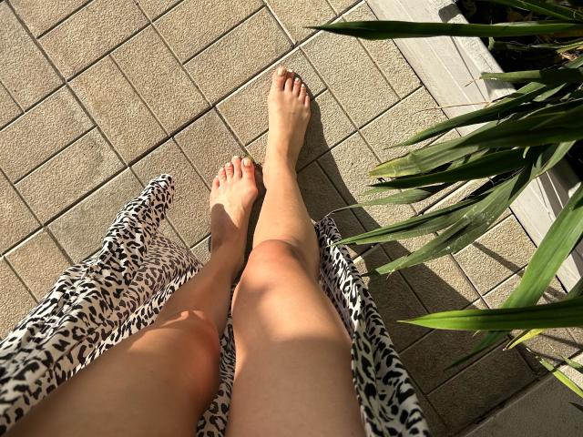 Karish's legs with bare feet on a zebra-patterned chair, sunlit, tan skin, green plant to the right, tiled floor, warm light, shadow on her knees.