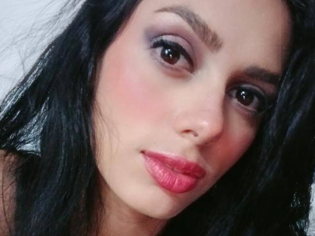 AnaisHilton has dark hair, pink lips, and smoky eye makeup. Her face is slightly tilted with a soft, sexy smile. She's looking at the camera with brown eyes.