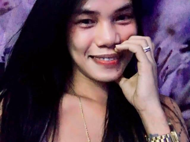 AsianIrishx with black hair, smiling, holding phone to ear, wearing gold necklace, ring, and watch, showing red lipstick and slightly blushed cheeks.