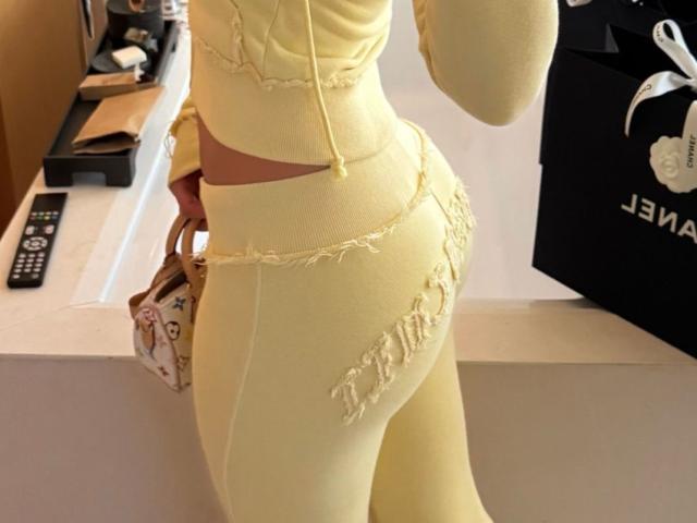 Arabia's yellow, fringed, tight-ass leggings and matching top, showing her curvy, butt-focused lower body, with a black shopping bag on the right and a remote on the left.