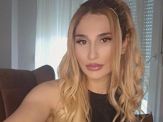 LaurinaxXx-hot has long blonde wavy hair, full pink lips, and is wearing a black top, showing her bare shoulders. She has a nose ring and is looking at the camera.