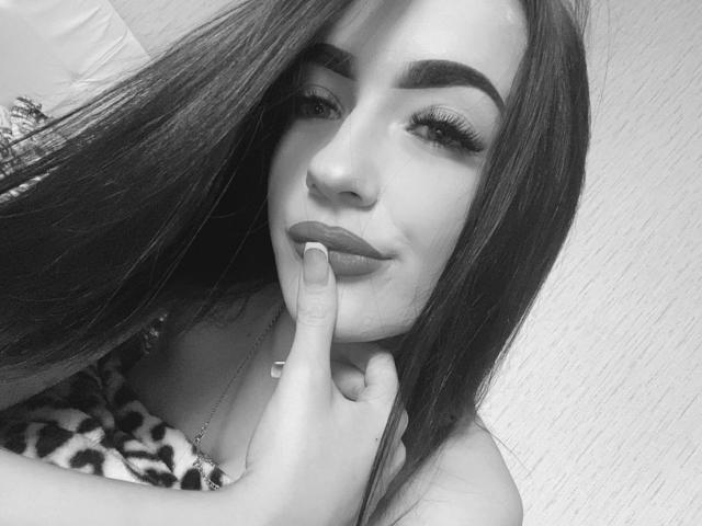 TuttiLily, con su largo cabello oscuro, cejas pobladas y labios carnosos, está tocándose la barbilla con un dedo. Lleva una blusa con estampado de leopardo y tiene pestañas largas y rizadas..